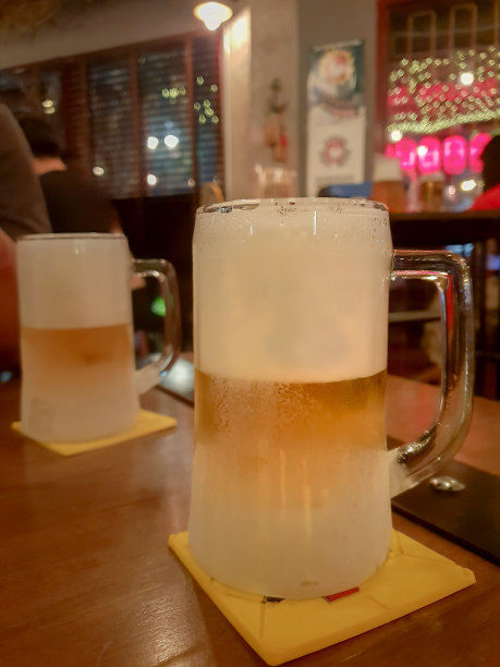 木制吧台上放着两杯冰镇啤酒，吧台的背景模糊了图片下载