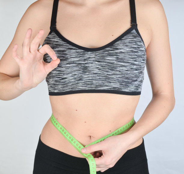 健身女孩在运动上衣测量尺腰围在白色的背景。减肥的概念。图片下载