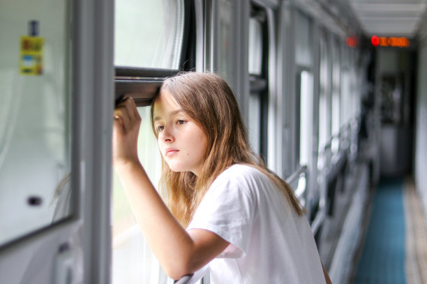 美丽沉思的十多岁的女孩看着悲伤的窗户在车厢里的火车悲伤离开。离别与离别的概念。图片下载