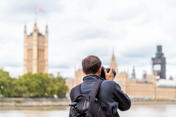英国伦敦，一名男子摄影师背着背包，三脚架拍摄，拍摄，拍摄城市天际线与泰晤士河，威斯敏斯特在多云的秋天在阿尔伯特堤岸图片下载