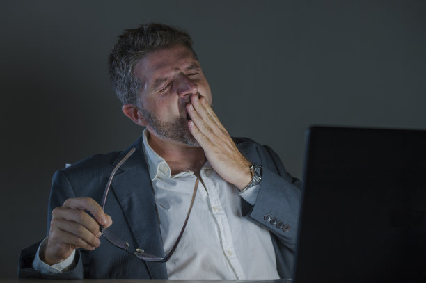 年轻的有吸引力的浪费和疲倦的企业家男人工作到深夜在办公室的笔记本电脑桌上打哈欠疲惫和困倦的金融业务问题和期限概念图片下载