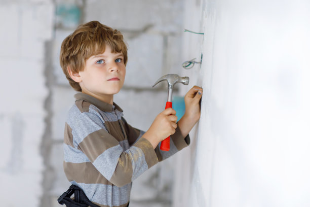一个小男孩在工地上帮忙拿玩具工具。6岁的有趣的孩子，在建立新的家庭的乐趣。孩子拿着钉子和锤子帮助父亲翻新旧房子。图片下载