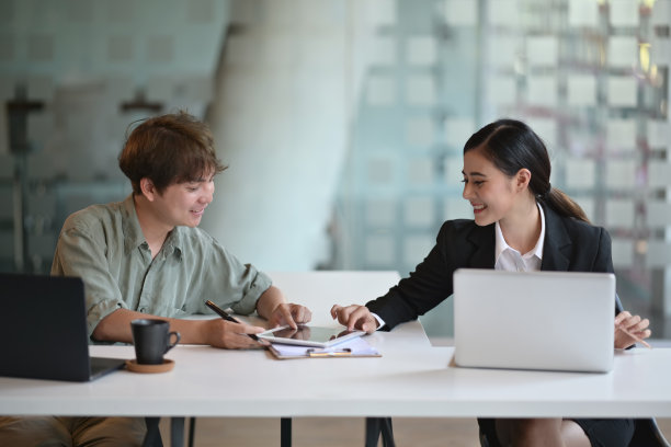 这是两名亚洲商业同事坐在办公场所，手里拿着平板电脑上的数据讨论工作的照片图片下载