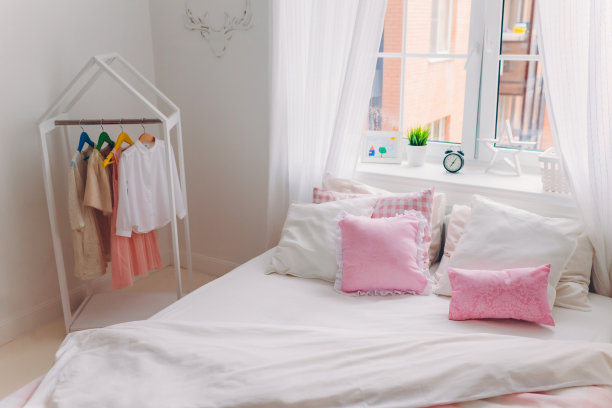 照片中的卧室空舒适宽敞，有大床，衣服挂在衣架上，窗户和白色窗帘。国内的气氛。室内拍摄图片下载