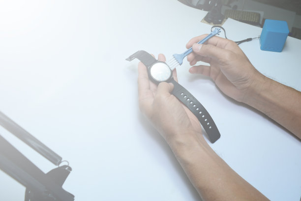 成人用手在白色工作台上用强光清洗黑色手表面板图片下载