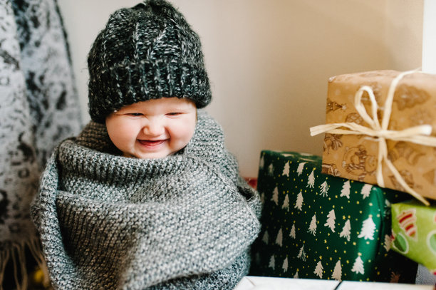 一个小女孩的肖像戴着温暖的针织帽子和围巾，坐在房间的背景礼物。节日生日的概念。照片里的婴儿。婴儿。妇女节。圣诞快乐，节日快乐。图片下载