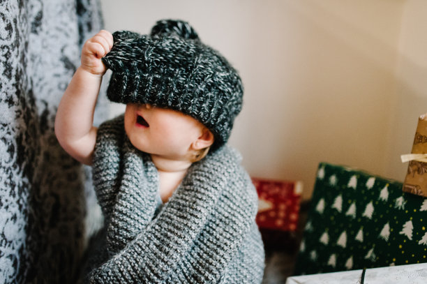 一个小女孩的肖像在一个温暖的针织围巾，脱下帽子，坐在房间的背景礼物。节日生日的概念。照片里的婴儿。婴儿。妇女节。圣诞快乐，节日快乐。图片下载