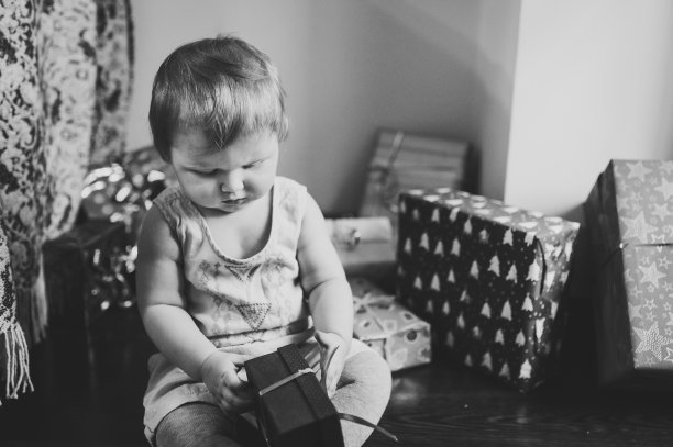 小女孩的肖像在房间里坐下并打开礼物。节日生日的概念。快乐宝宝黑白照片。婴儿。妇女节，三月八日。圣诞快乐，节日快乐。新年。图片下载