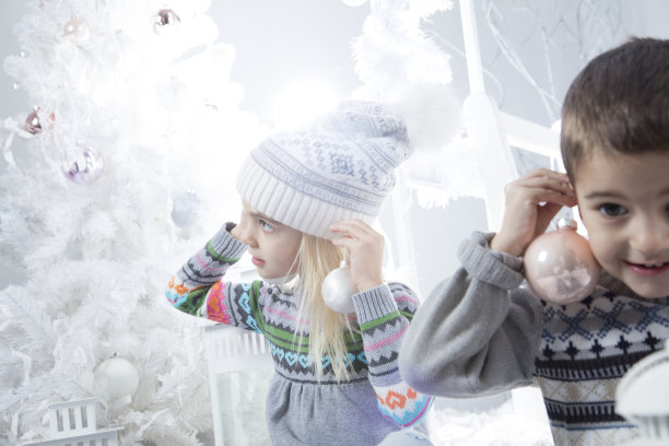 女孩和男孩坐在家里的圣诞树旁，耳朵上挂着一个球状的装饰品图片下载