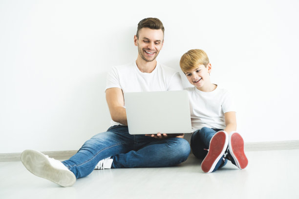 父亲和儿子拿着笔记本电脑坐在地板上图片下载