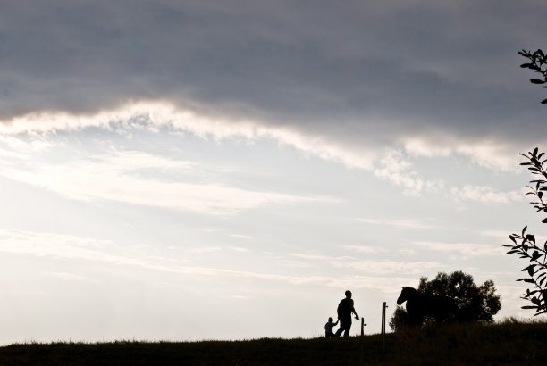 一个父亲和一个孩子在动物农场的剪影。乌云背景图片下载