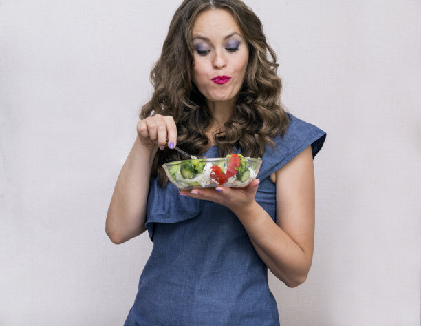 一个穿着蓝色连衣裙的卷发女孩吃着蔬菜沙拉，是白人年轻女子图片下载