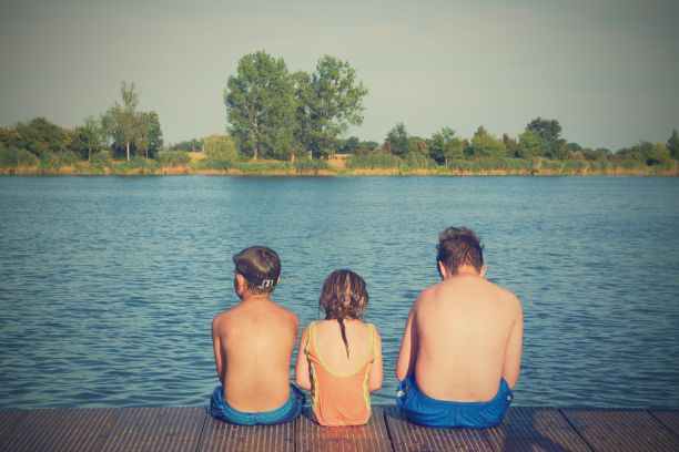 孩子们坐在码头上。三个不同年龄的孩子——十几岁的男孩、小学年龄的男孩和学龄前的女孩坐在一个木码头上。夏季和童年的概念。孩子们坐在湖边的长椅上。兄弟姐妹坐在木码头上图片下载