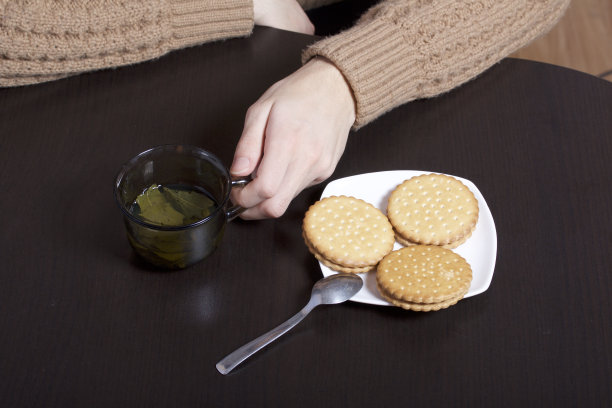 一个年轻人喝绿茶和饼干。茶倒进玻璃杯里，饼干躺在人身上。图片下载