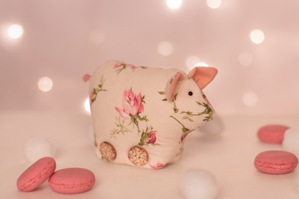 在圣诞彩灯、粉色通心粉和软球的背景下，这只手工制作的粉色花朵小猪站了起来图片下载