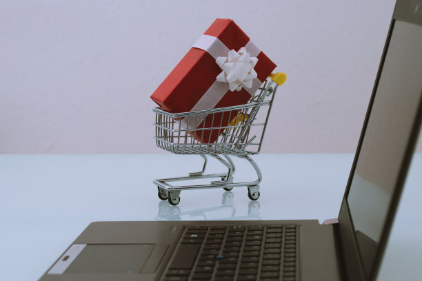 小手推车，红色礼物和黑色电脑。通过网上电子商务购买产品。最后一分钟的圣诞网上购物概念。图片下载