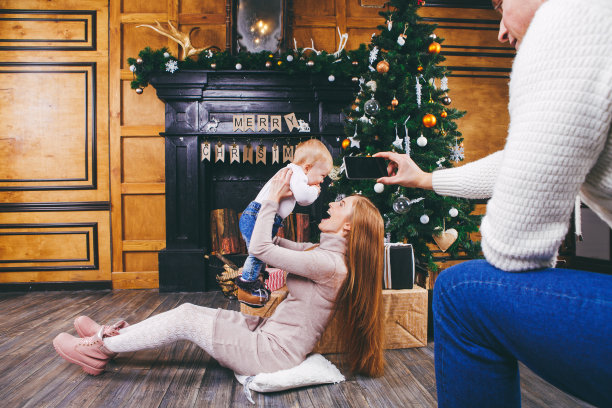 主题手机摄影，业余摄影视频手机。手白种男子持有使用智能手机使照片母子家壁炉和圣诞树附近的冬季圣诞新年装饰图片下载