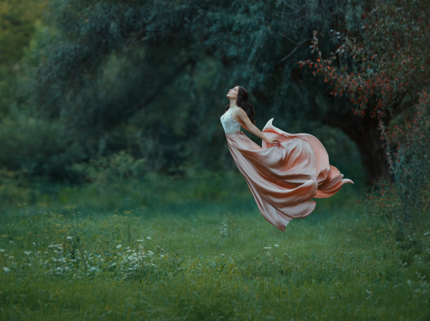 年轻苗条的女子，黑头发，整洁的头发，穿着长长的豪华的飘扬的飞行服在空中。图片下载