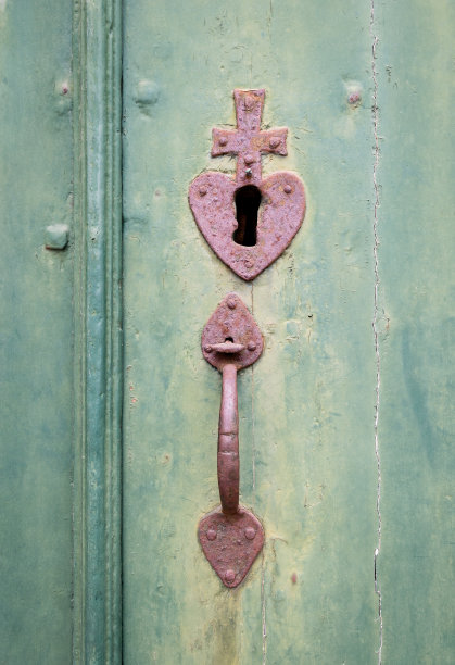 老式的钥匙孔和门把手上有一个心和十字在一个旧的门。图片下载