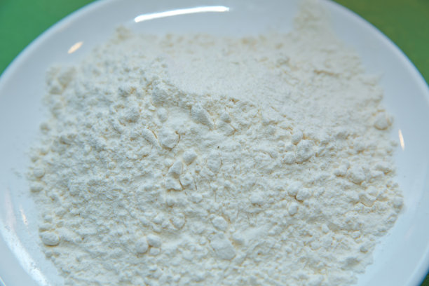 面粉在盘子的绿色背景。特写小麦粉堆粗在白色盘子上绿色的背景。留在照片上。部分奶粉特写镜头，绿色背景图片下载