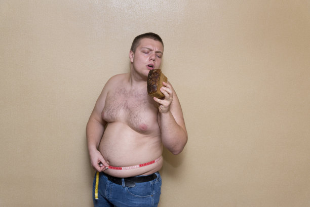 一个男人用一米测量他肥胖的肚子，一只手拿着面包图片下载