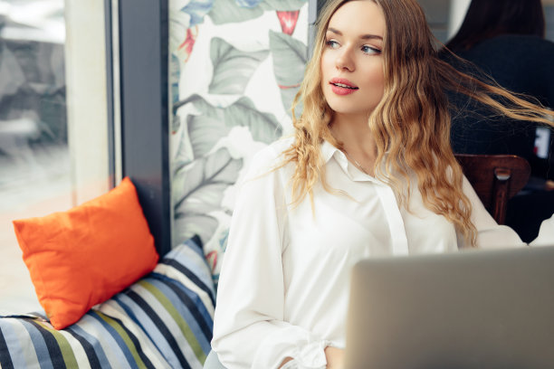 女人戴着眼镜，在咖啡馆用笔记本电脑工作时喝着热咖啡。肖像时尚微笑的女人在冬天的衣服喝热咖啡和工作在笔记本电脑。女性冬季风格。——图片图片下载