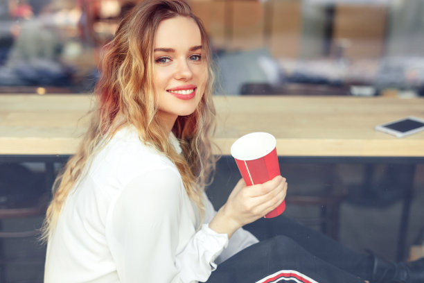 坐在咖啡馆里喝热咖啡的女人。肖像时尚微笑的女人在冬天的衣服喝热咖啡。女性冬季风格。——图片图片下载