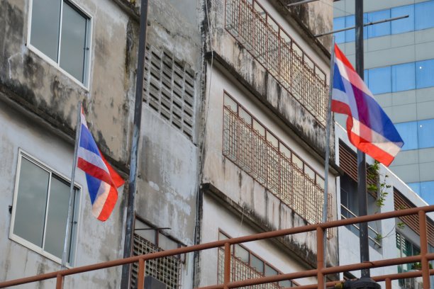 曼谷一幢建筑顶上的旗杆上，两面泰国国旗在风中飘扬图片下载