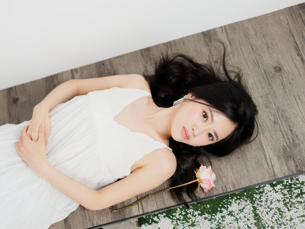 俯视图，一个美丽的中国女孩躺在地板上，双手放在身体上，对着镜头微笑，浪漫的年轻女性的肖像。图片下载