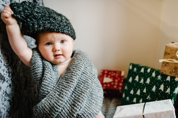 一个小女孩的肖像在一个温暖的针织围巾，脱下帽子，坐在房间的背景礼物。节日生日的概念。照片里的婴儿。婴儿。妇女节。圣诞快乐，节日快乐。图片下载