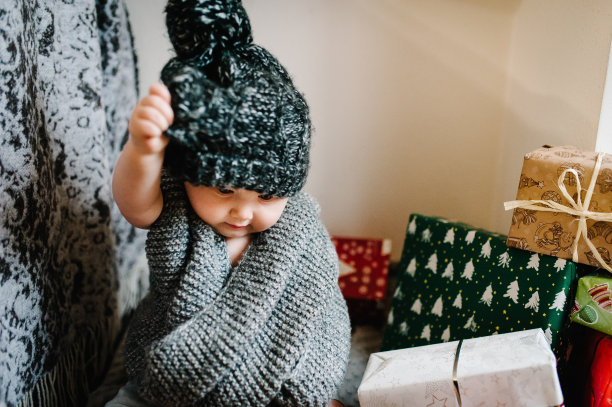 一个小女孩的肖像在一个温暖的针织围巾，脱下帽子，坐在房间的背景礼物。节日生日的概念。照片里的婴儿。婴儿。妇女节。圣诞快乐，节日快乐。图片下载
