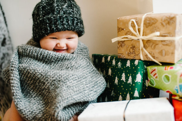 一个小女孩的肖像戴着温暖的针织帽子和围巾，坐在房间的背景礼物。节日生日的概念。照片里的婴儿。婴儿。妇女节。圣诞快乐，节日快乐。图片下载