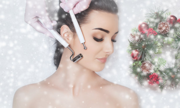 美容师在美容院为一位美女做微电流治疗。特写女人的脸和用雪花装饰的新年花环。图片下载