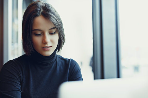 女人在咖啡馆用笔记本电脑工作时环顾四周并微笑。一个穿着冬装在笔记本电脑前工作的时尚微笑女人的肖像。女性与太阳的商务风格。——图片图片下载