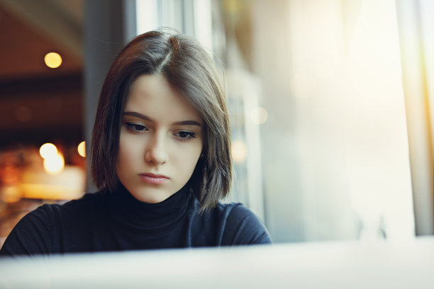 女人在咖啡馆用笔记本电脑工作时环顾四周并微笑。一个穿着冬装在笔记本电脑前工作的时尚微笑女人的肖像。女性与太阳的商务风格。——图片图片下载