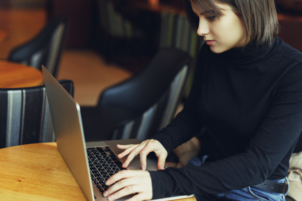 女人在咖啡馆用笔记本电脑工作时环顾四周并微笑。一个穿着冬装在笔记本电脑前工作的时尚微笑女人的肖像。女性与太阳的商务风格。——图片图片下载