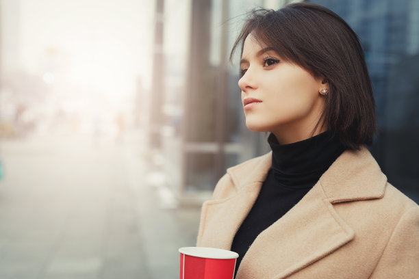 女人一边走在街上一边喝着热咖啡。肖像时尚微笑的女人在冬天的衣服喝热咖啡。女性冬季风格。——图片图片下载