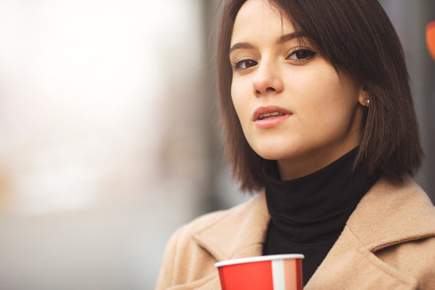 女人一边走在街上一边喝着热咖啡。肖像时尚微笑的女人在冬天的衣服喝热咖啡。女性冬季风格。——图片图片下载