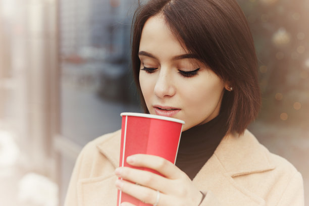 女人一边走在街上一边喝着热咖啡。肖像时尚微笑的女人在冬天的衣服喝热咖啡。女性冬季风格。——图片图片下载