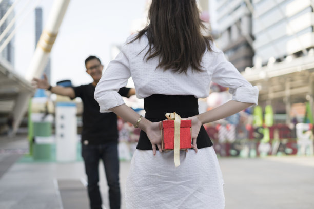 情侣送礼物的概念。女人背后拿着礼物，想在特别的日子给男友一个惊喜。家庭和爱人的观念。生日和情人节主题。图片下载