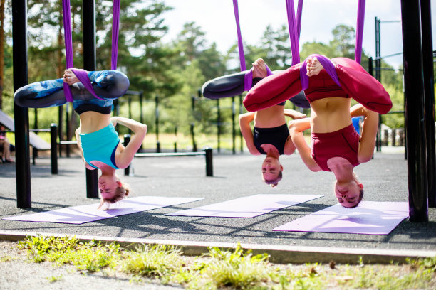 一群年轻女子在户外紫色吊床上做空中瑜伽练习。在吊床上飞行图片下载