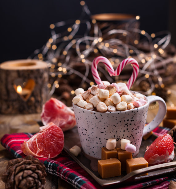 白色杯子里放着可可和棉花糖，木制背景上放着不同的圣诞糖果和糖果。照片在黑暗的风格和自由的文字空间。蜡烛和节日装饰品。明信片和问候。图片下载