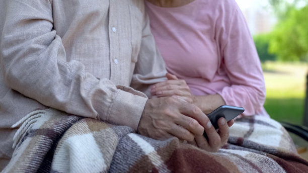 老祖父母在智能手机上看家庭照片，在公园里放松，小玩意图片下载