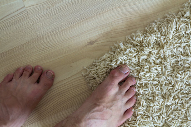 人们光着脚站在地板上。一只脚踩在地毯上，另一只脚踩在复合木地板上图片下载