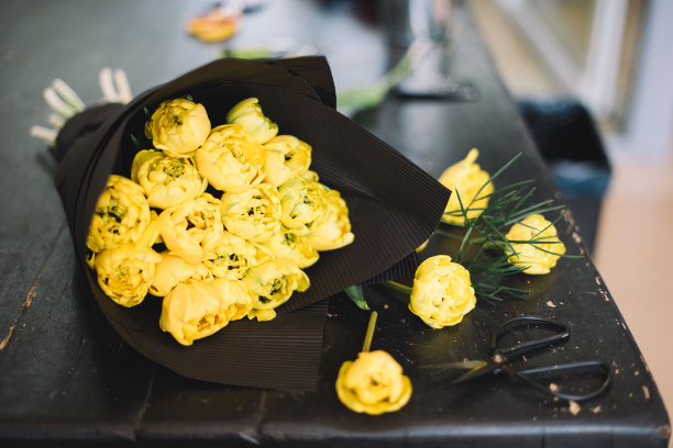 花店的木桌上放着一束用黑色纸包着的黄色郁金香图片下载