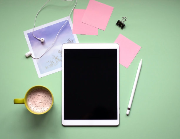 绿色背景的触控笔平板电脑。一杯咖啡，耳机，照片。图片下载