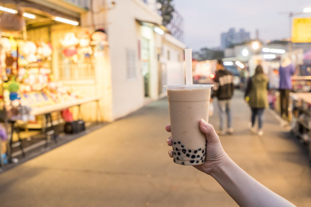 台湾夜市上，一名年轻女子正用吸管拿着一杯泡沫奶茶，台湾美食，特写。素材图片