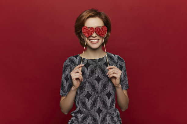 美丽开朗的年轻时尚模特女孩与情人节心的棍子在手中。爱。穿着漂亮衣服的年轻女子。情人节礼物。红色的背景。——图片图片下载
