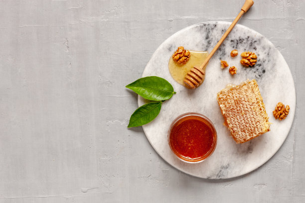玻璃锅，新鲜的天然蜂蜜，蜂窝和核桃放在石板上。俯视图，特写，平铺在灰色混凝土背景上图片下载