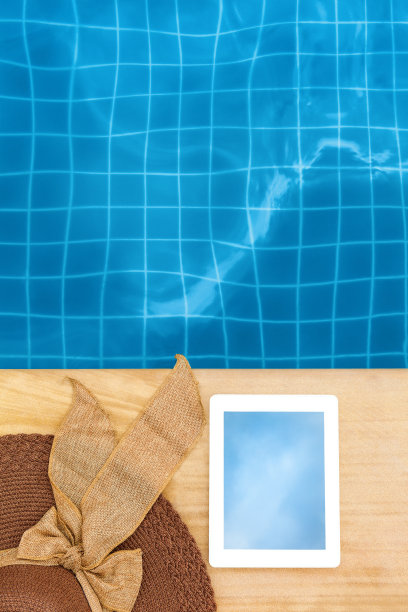 写字板和太阳帽在蓝色游泳池附近图片下载
